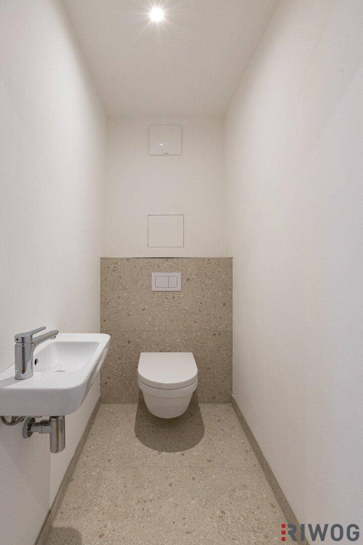 Kleines Gäste-WC mit wandhängender Toilette, kleinem Waschbecken und modernen Fliesen.