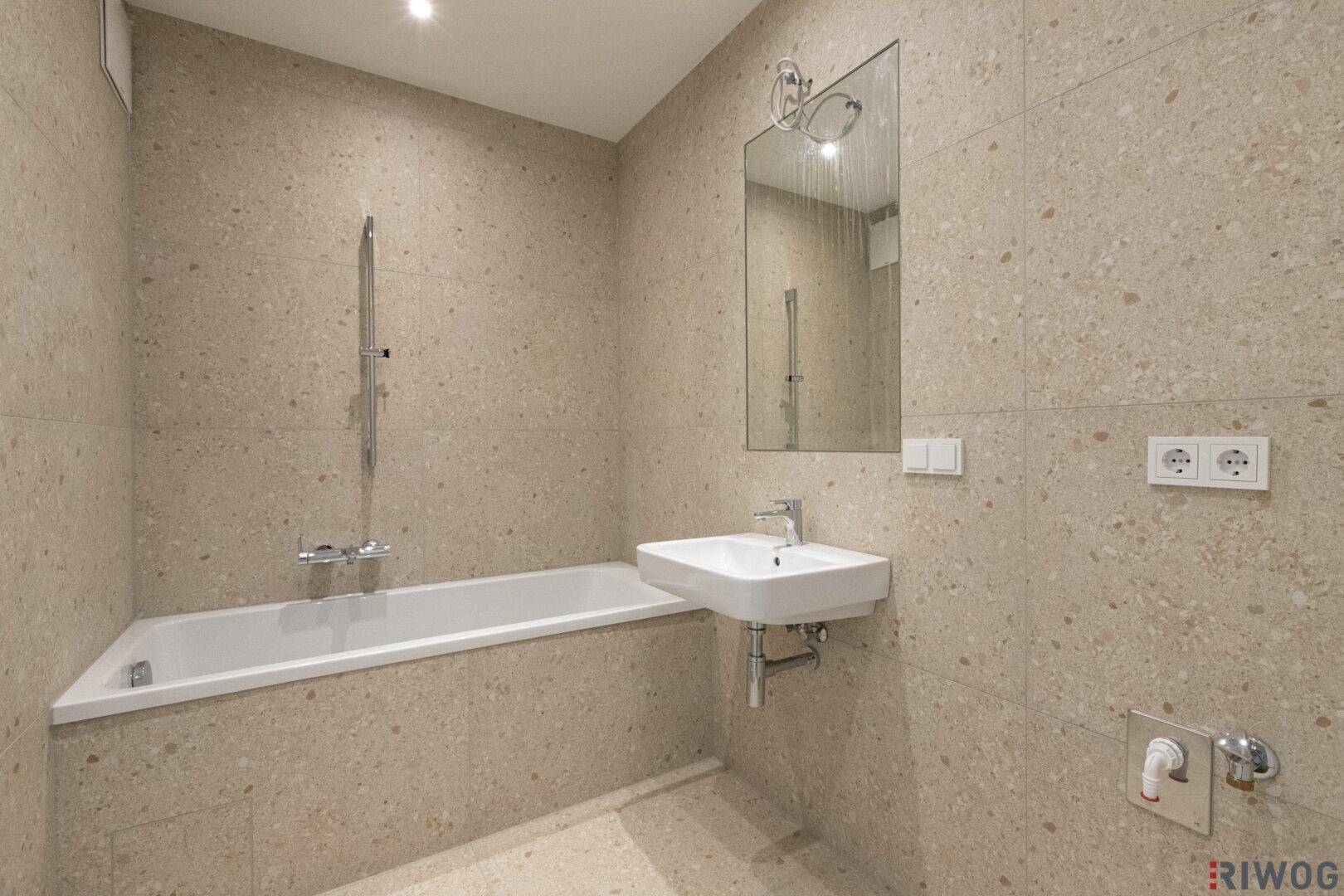 Modernes Badezimmer mit beigefarbenen Fliesen, Badewanne mit Duschfunktion und Einzelwaschbecken.
