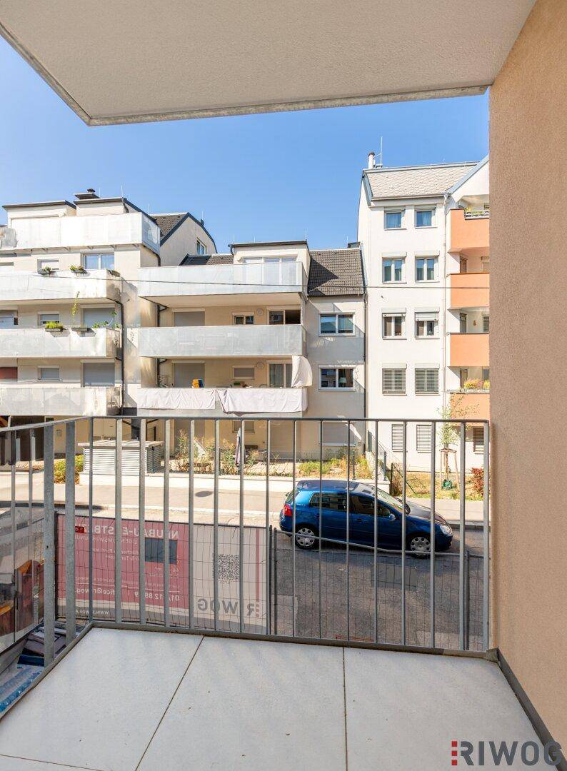 Balkon mit Metallgeländer und Blick auf die Straße sowie die gegenüberliegenden Gebäude.