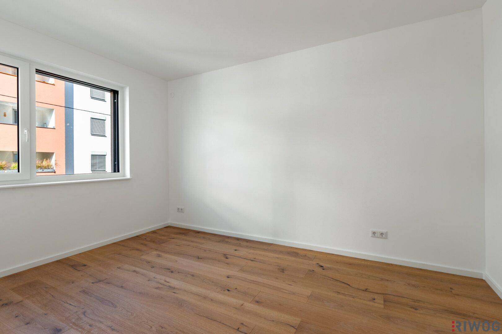 Leeres Zimmer mit Holzboden und weiß gestrichenen Wänden, ideal als Schlaf- oder Arbeitszimmer.