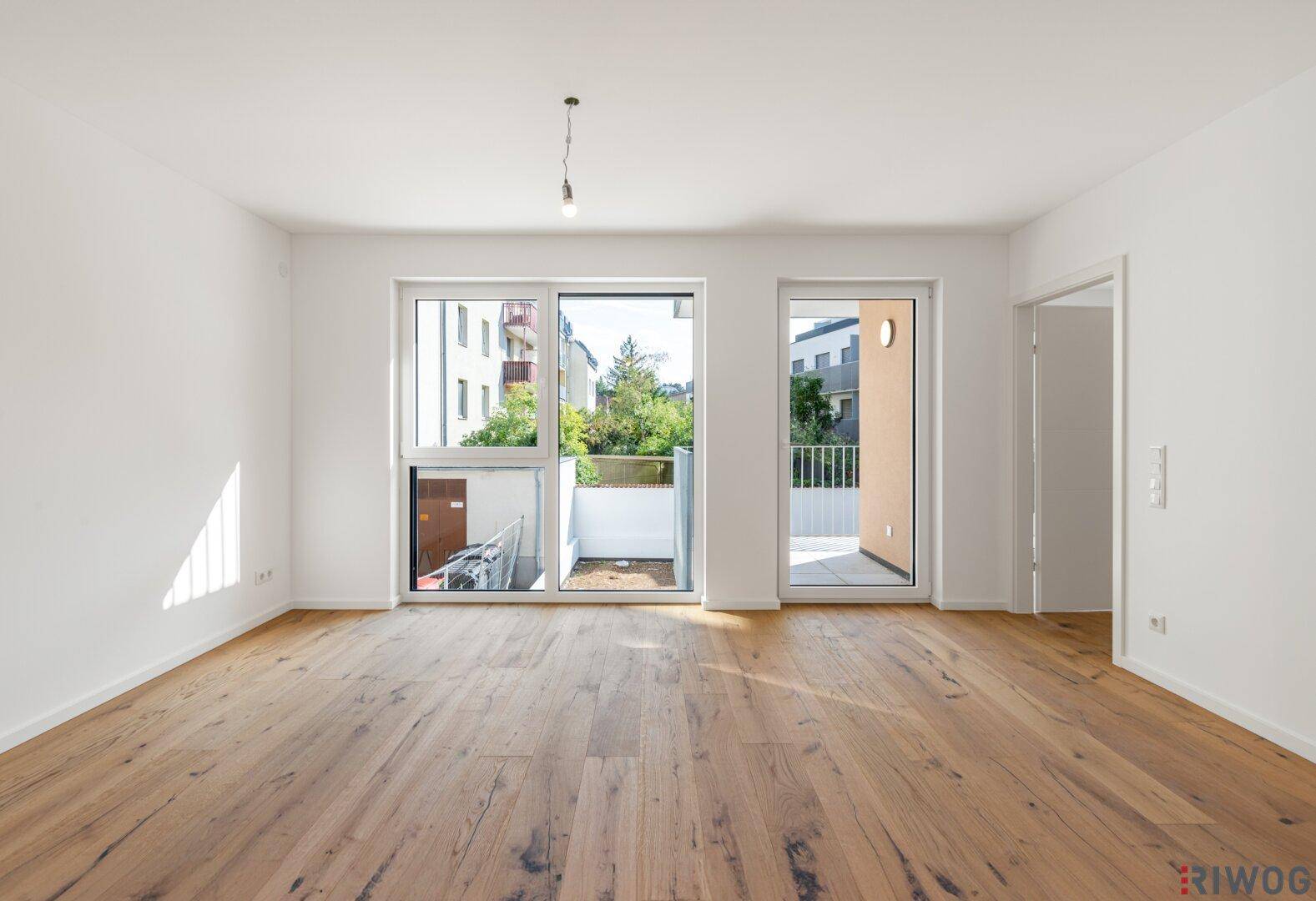 Geräumiger, heller Raum mit Holzboden und Zugang zu einem Außenbereich durch große Fenster.