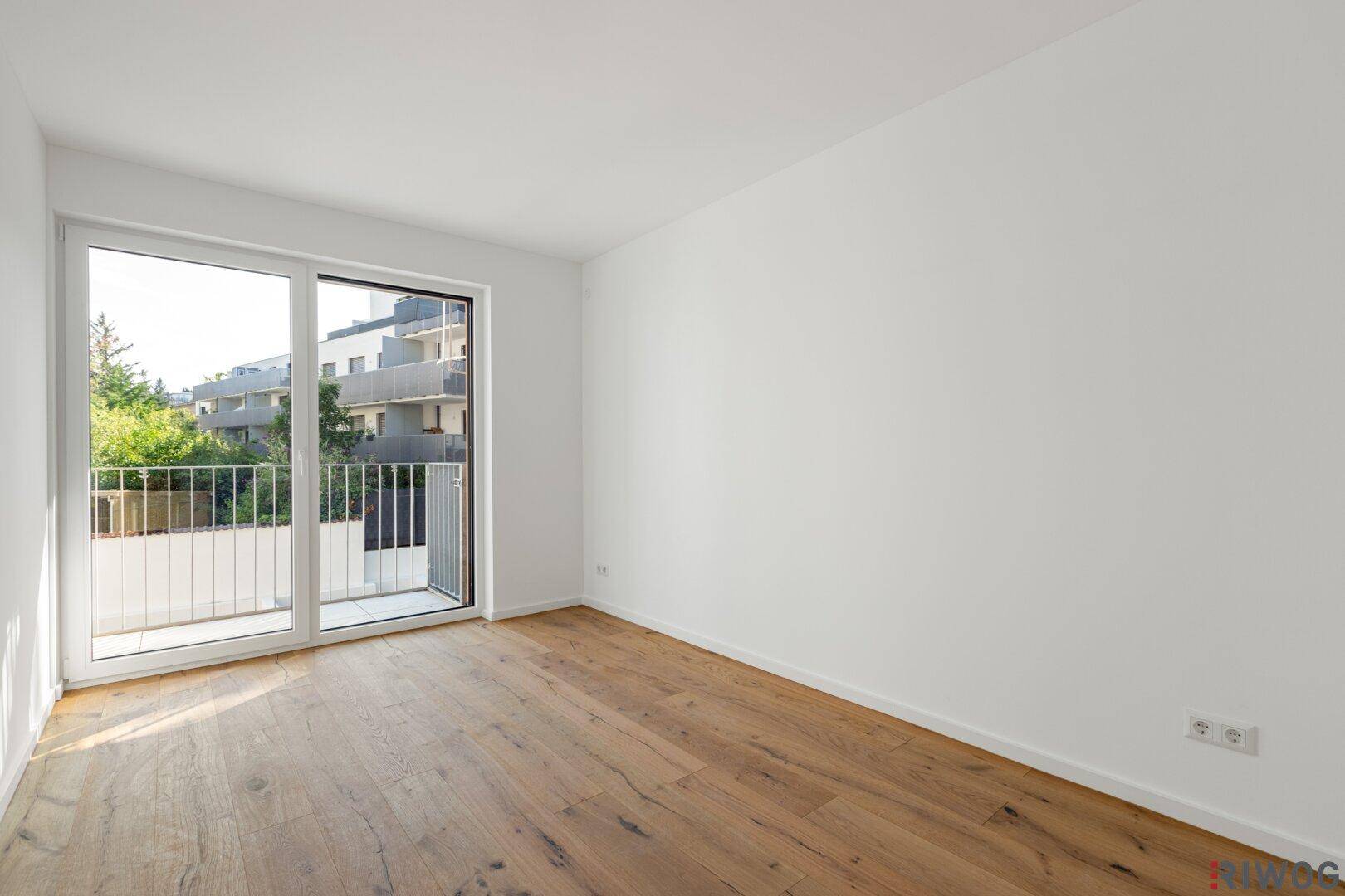 Heller Raum mit Holzboden und Zugang zu einem Balkon durch eine große Fenstertür.