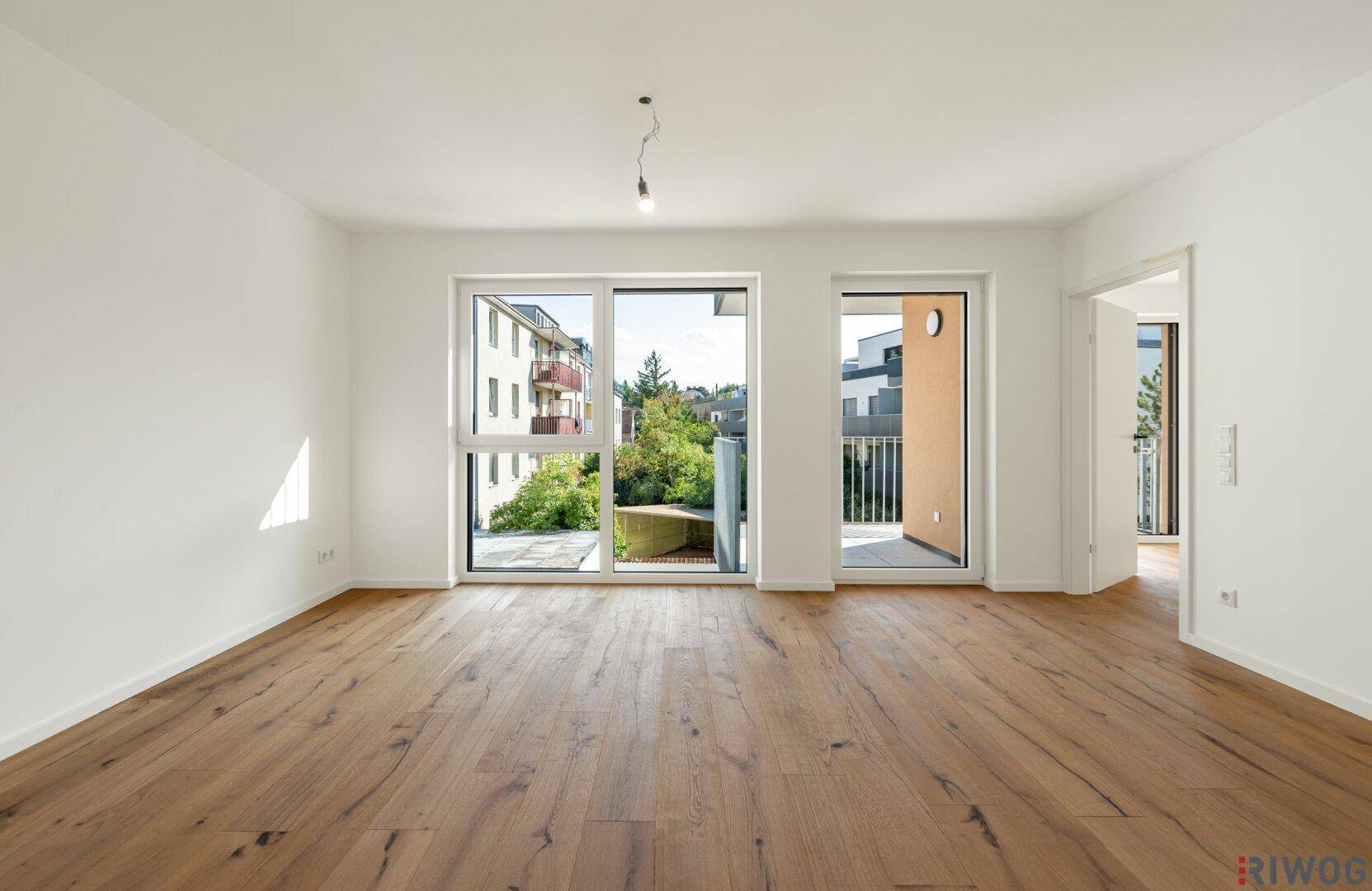 Geräumiges, leeres Wohnzimmer mit hochwertigem Holzboden und viel Tageslicht.