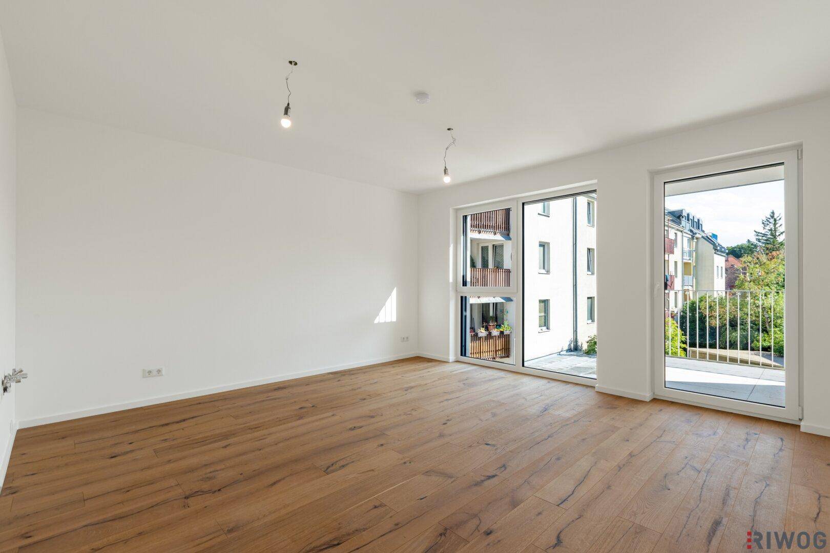 Heller, unmöblierter Raum mit Holzboden und Zugang zu einem Balkon.