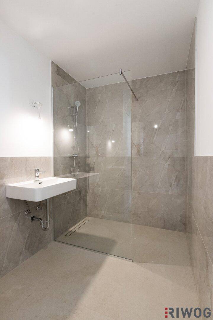 Modernes Badezimmer mit begehbarer Dusche, Wandwaschbecken und grauen Fliesen.
