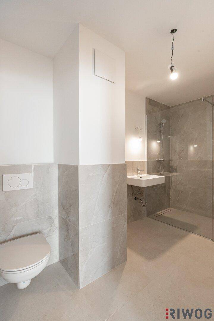 Modernes Badezimmer mit wandhängendem WC, Waschbecken und begehbarer Dusche.