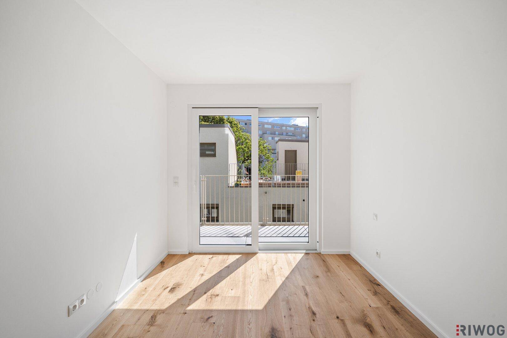Freundlicher Raum mit Holzboden und breiter Schiebetür, die den Zugang zum Balkon ermöglicht.