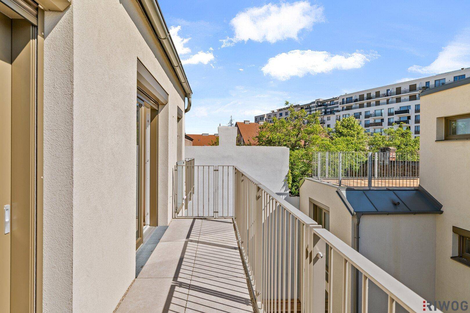 Schmaler Balkon mit Metallgeländer und Blick auf die umliegenden Gebäude und Grünflächen.