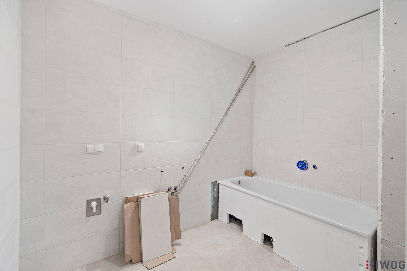 Unfertiges Badezimmer mit weißen Fliesen und eingebauter Badewanne, bereit für die Endmontage.
