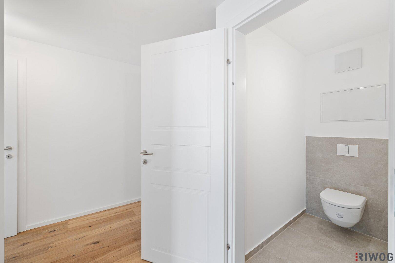 Modernes Gäste-WC mit wandhängender Toilette und grauen Fliesen im unteren Bereich.