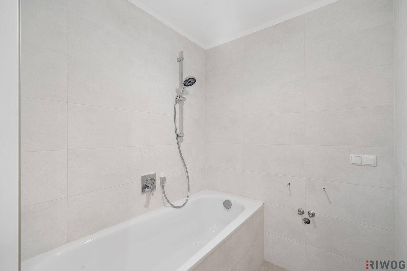 Modernes Badezimmer mit Badewanne und integrierter Duschfunktion, hell gefliest.