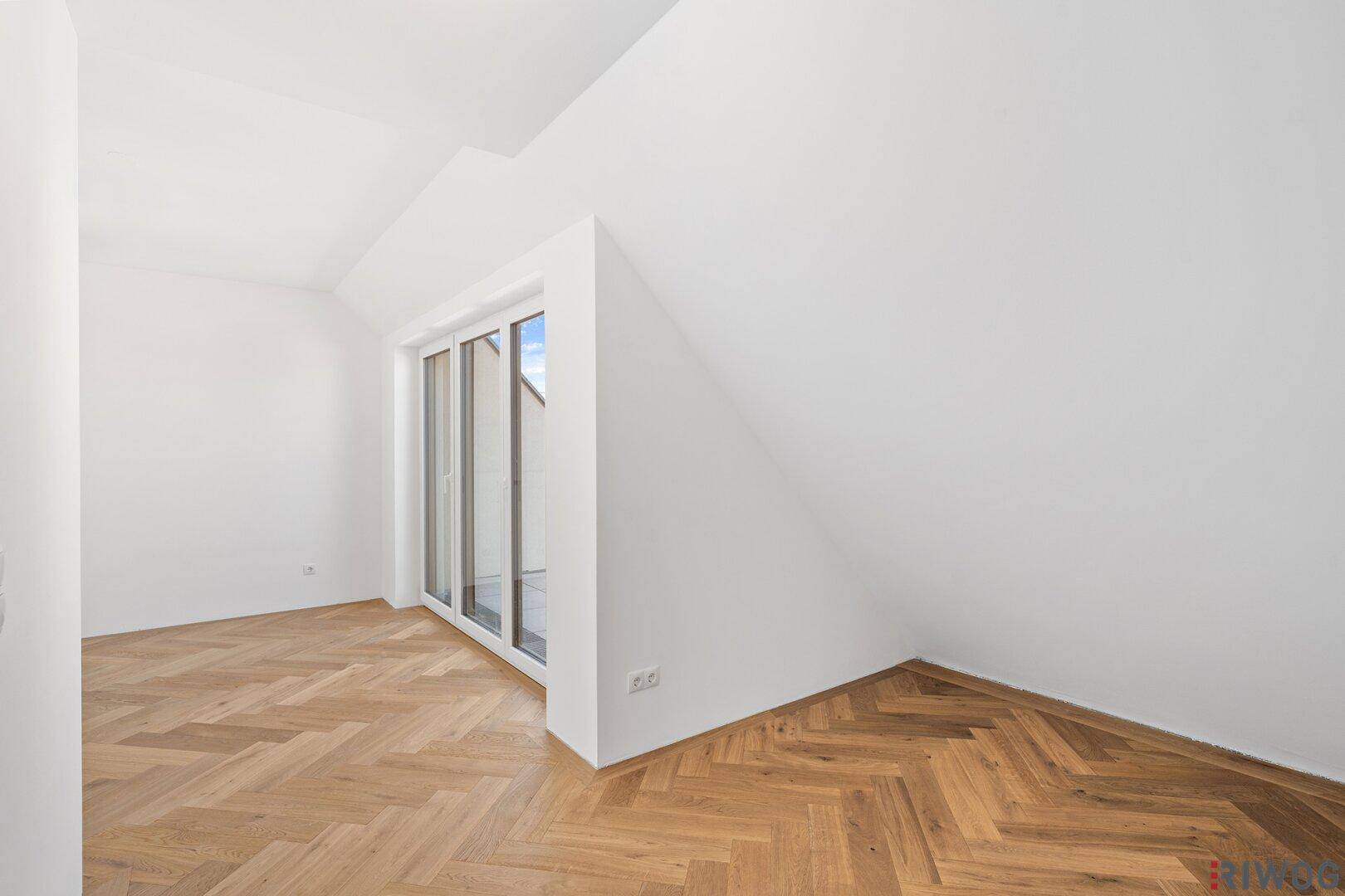 Helles Zimmer im Dachgeschoss mit Fischgrätparkett und Zugang zu einem Balkon.