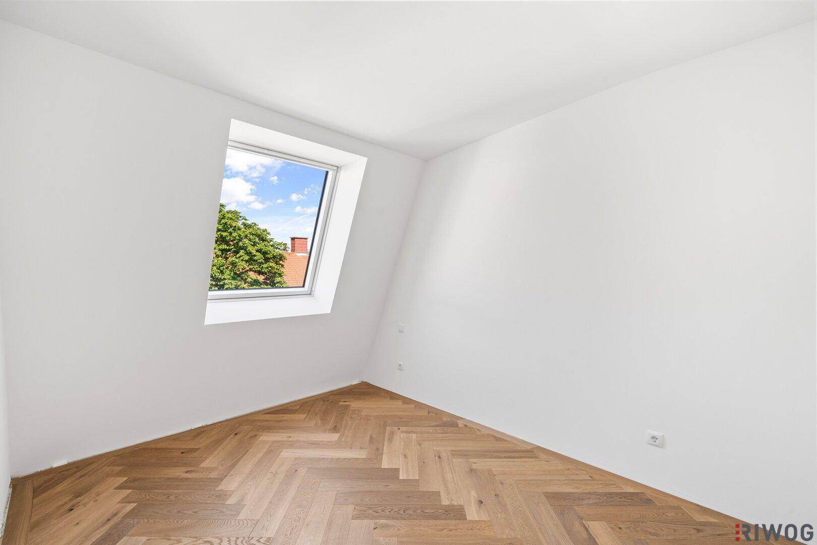 Helles Dachgeschosszimmer mit Fischgrätparkett und einem schrägen Dachfenster.