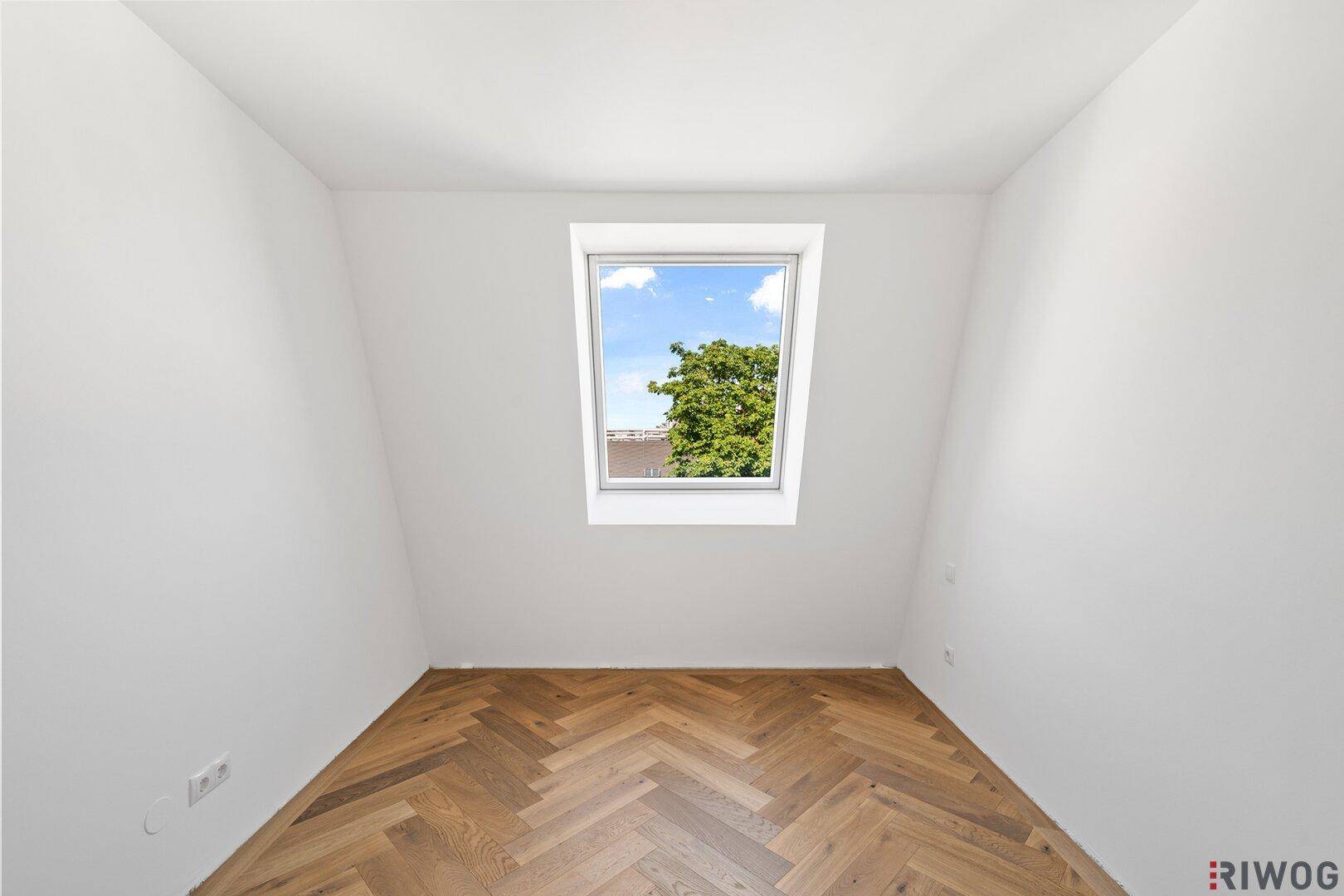 Gemütliches Dachgeschosszimmer mit Fischgrätparkett und einem schrägen Dachfenster.