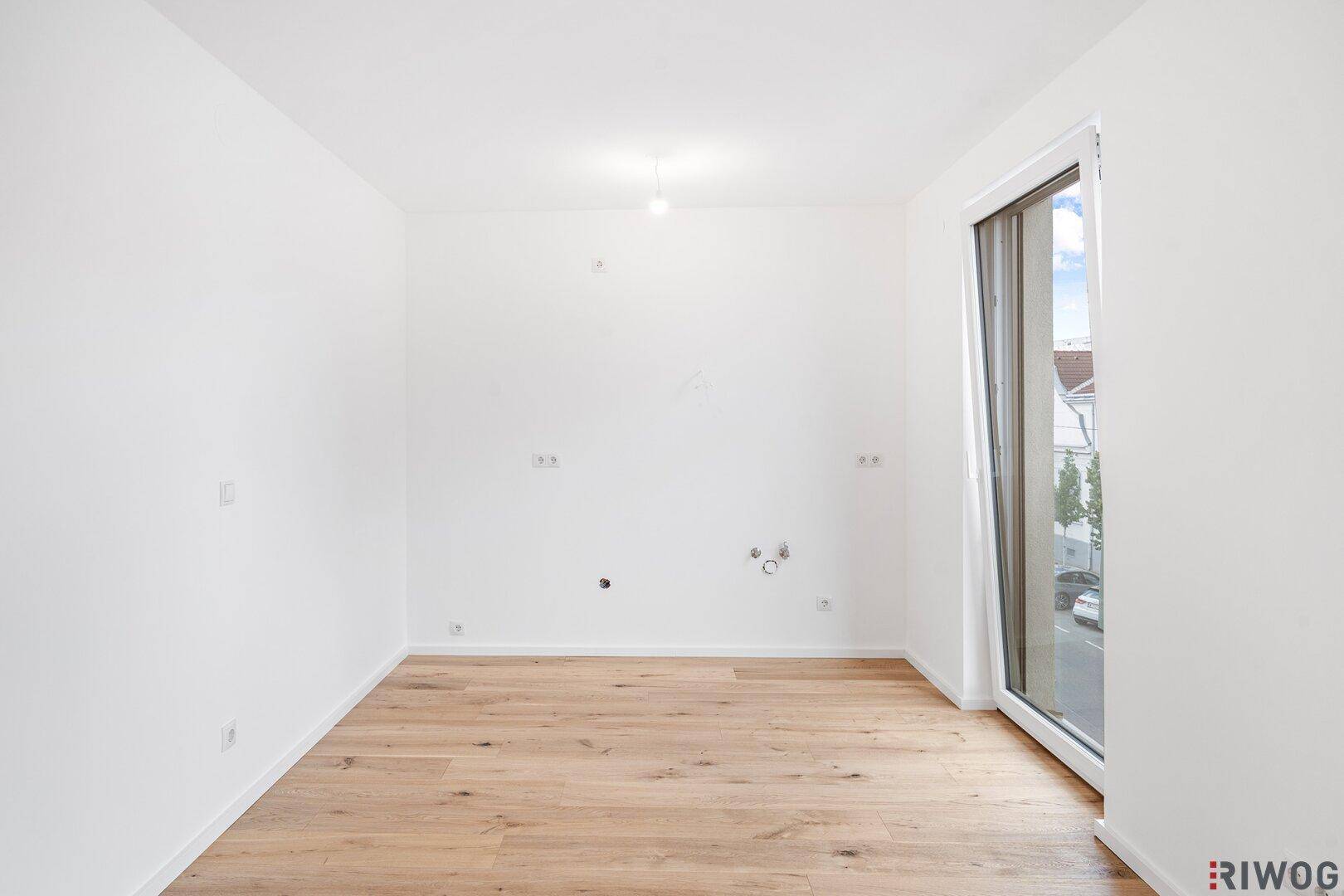 Leeres Zimmer mit hellem Holzboden und einer Tür, die nach draußen führt.