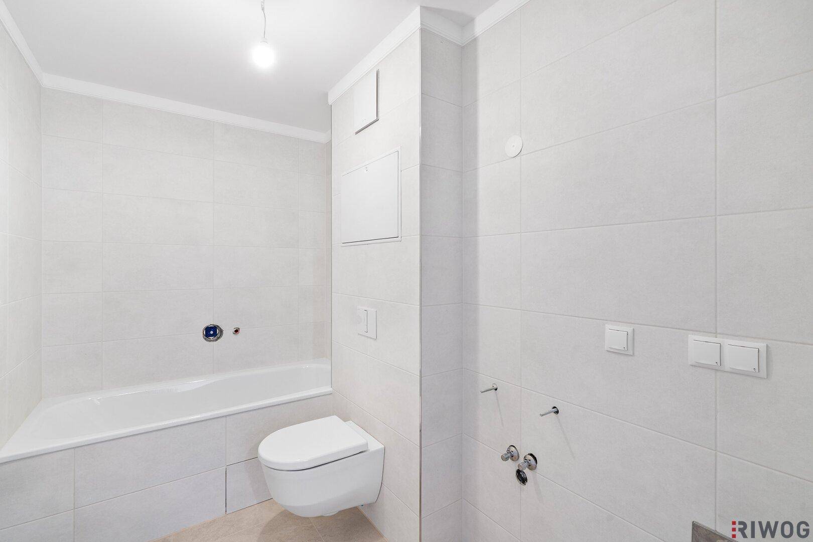 Modernes Badezimmer mit weißen Fliesen, Badewanne und wandhängendem WC.