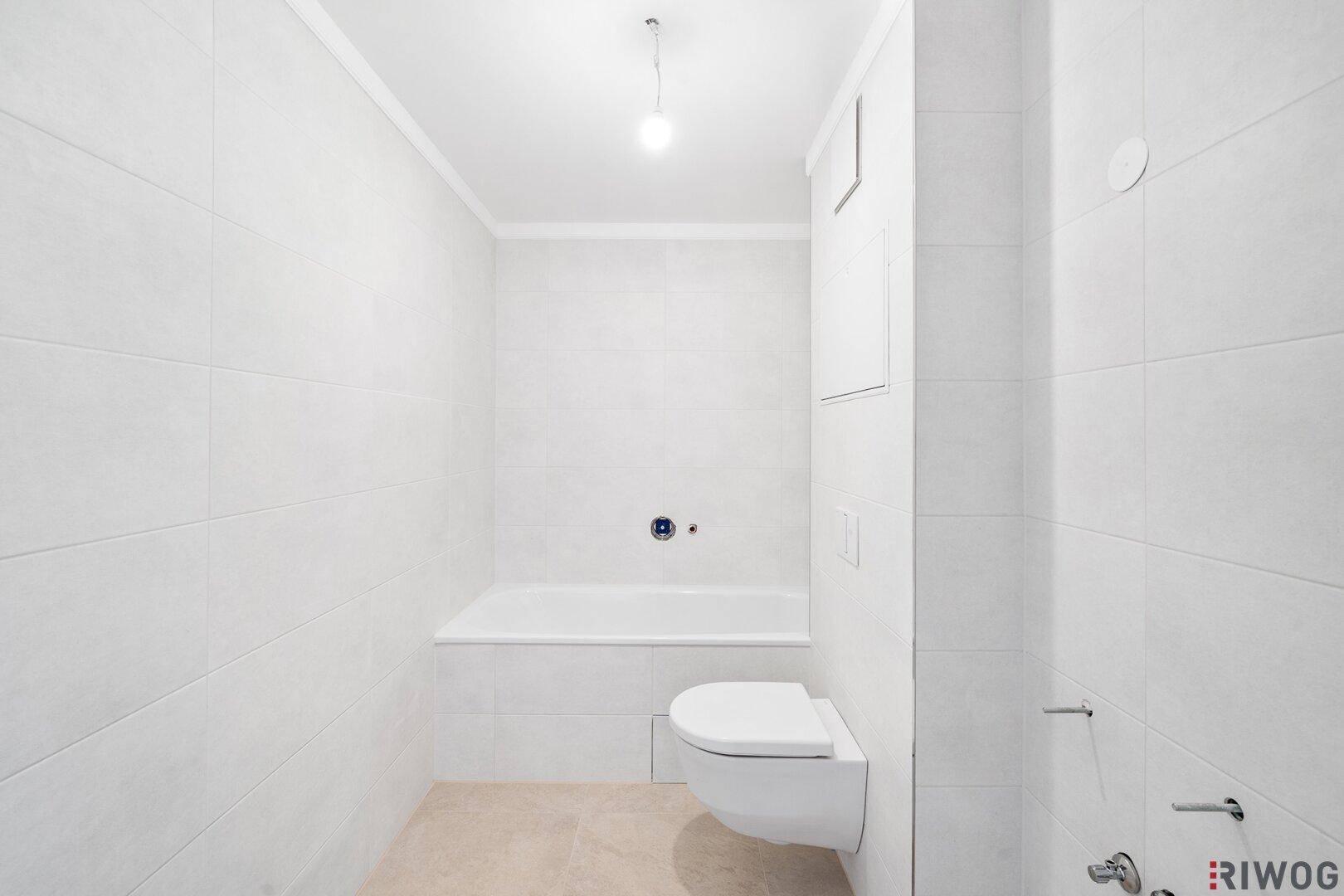 Helles Badezimmer mit weißen Fliesen, Badewanne und wandhängender Toilette.