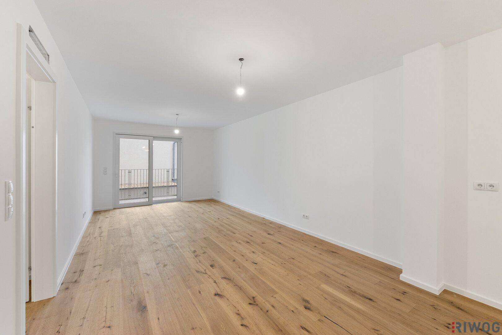 Heller Wohnraum mit Holzboden und Zugang zu einem Balkon durch eine große Glasschiebetür.