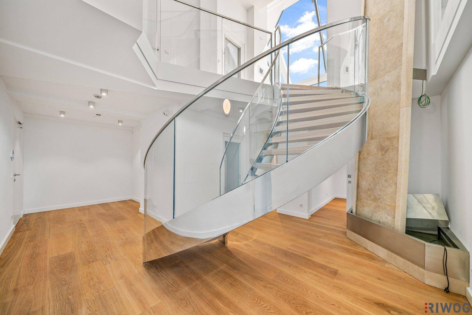 Elegante Wendeltreppe aus Glas und Holz in einem hellen Eingangsbereich mit Holzboden.