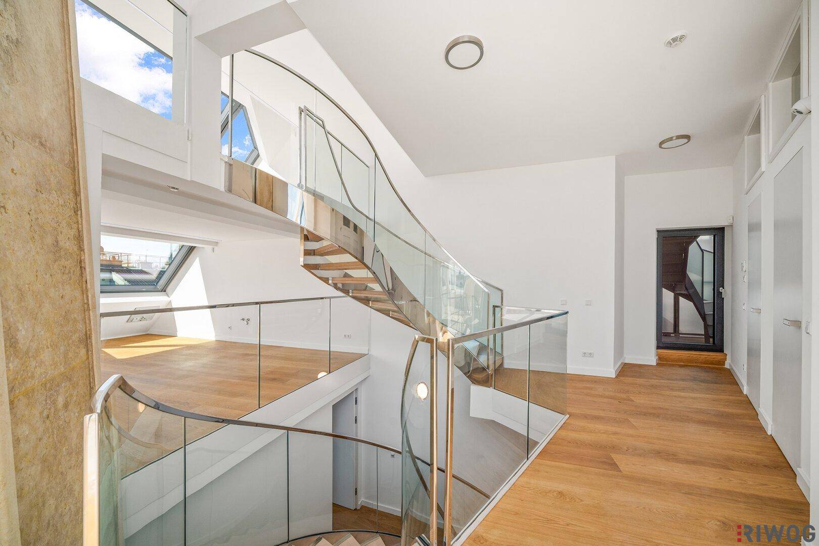 Heller Flur mit Holzboden, Einbauschränken und einer eleganten Wendeltreppe mit Glasgeländer.