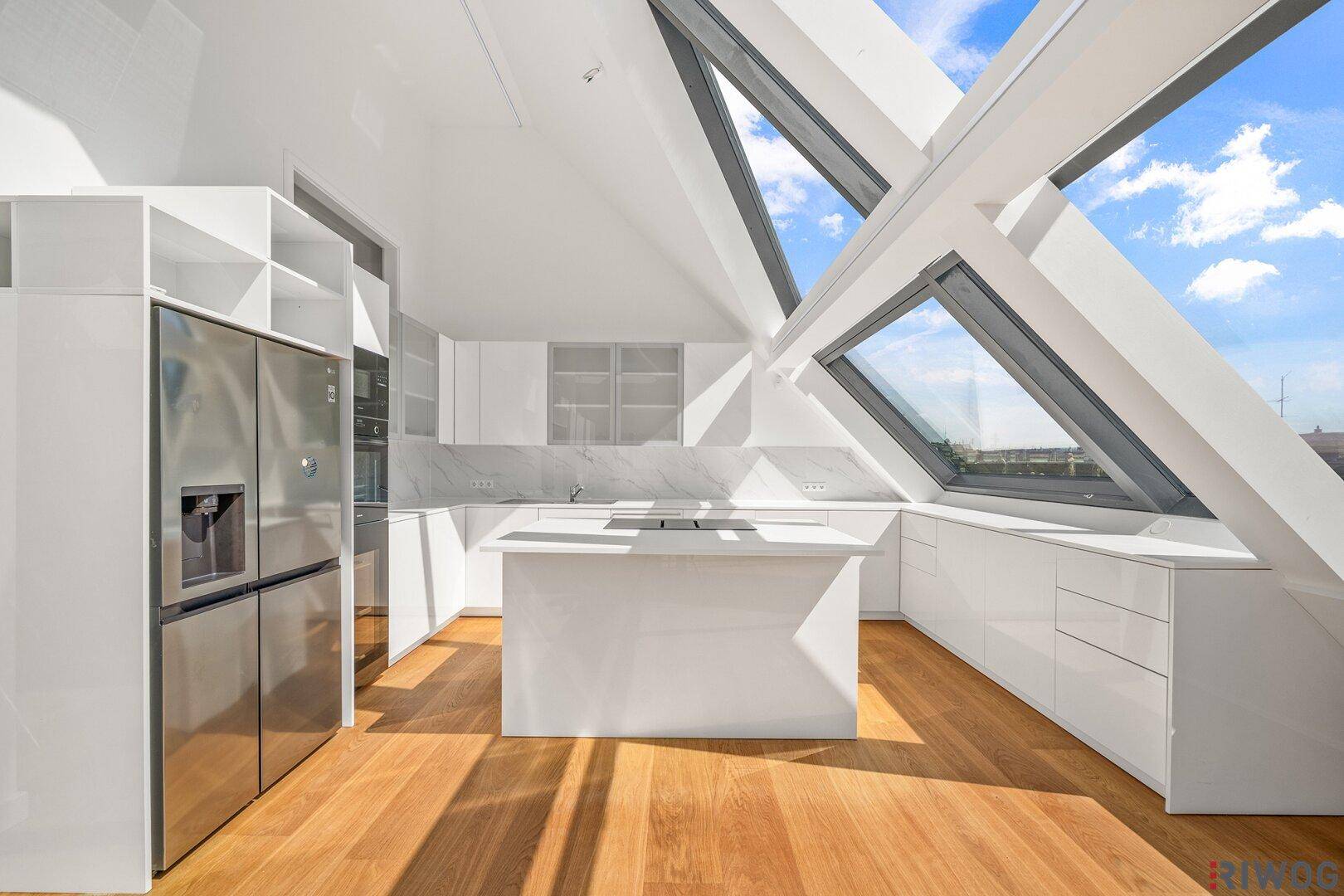 Moderne weiße Küche mit Kücheninsel, großem Kühlschrank und schrägen Dachfenstern.
