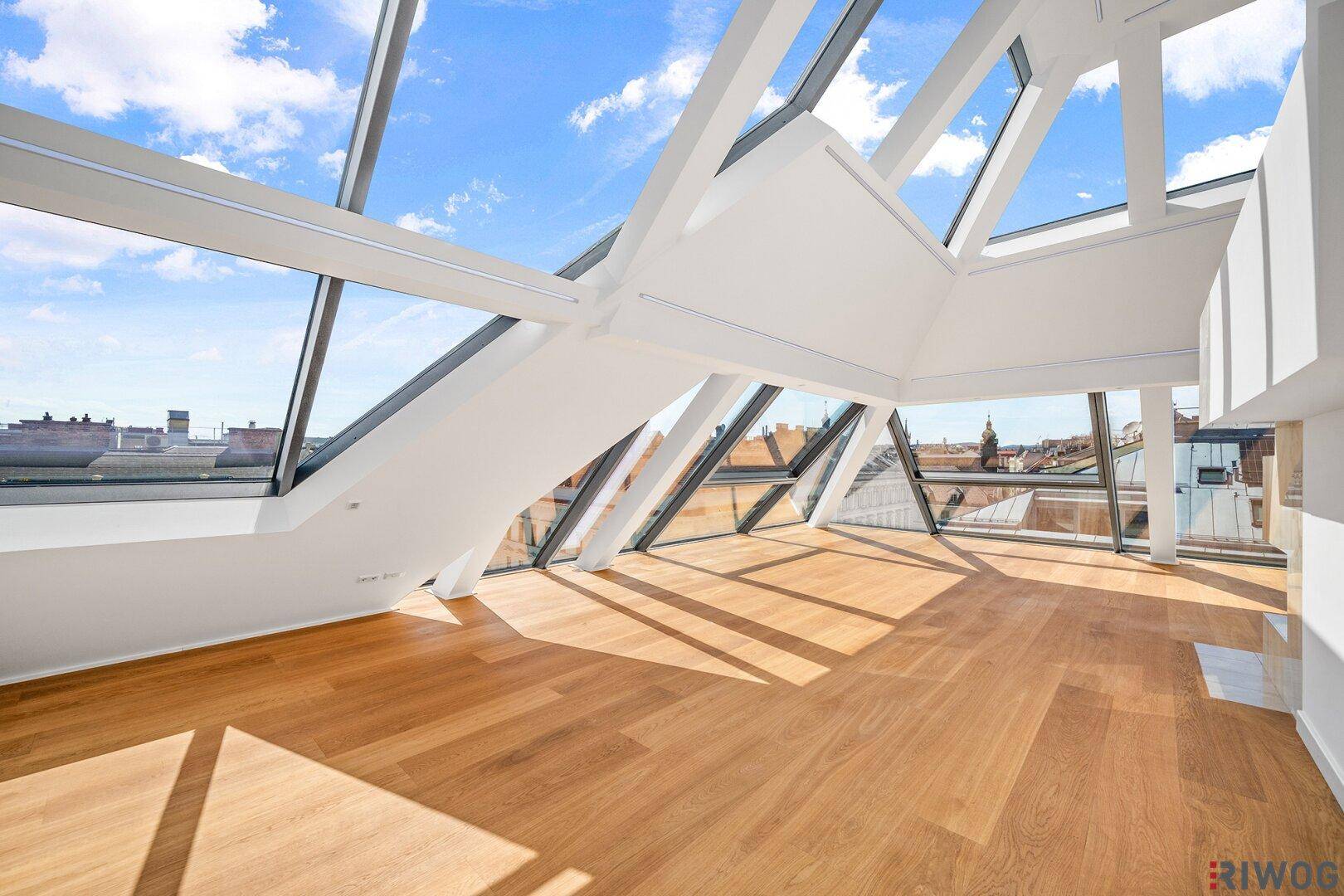 Heller Wohnbereich mit Holzboden und großen schrägen Fenstern, die einen weiten Stadtblick bieten.