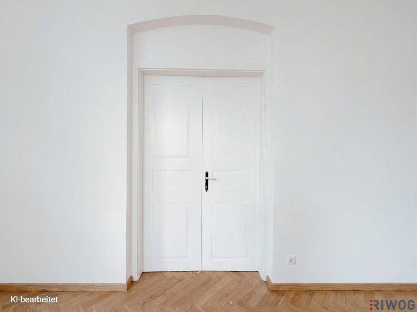 Elegante weiße Doppeltür mit Bogenrahmen und Fischgrätparkett, ein klassisches architektonisches Detail.