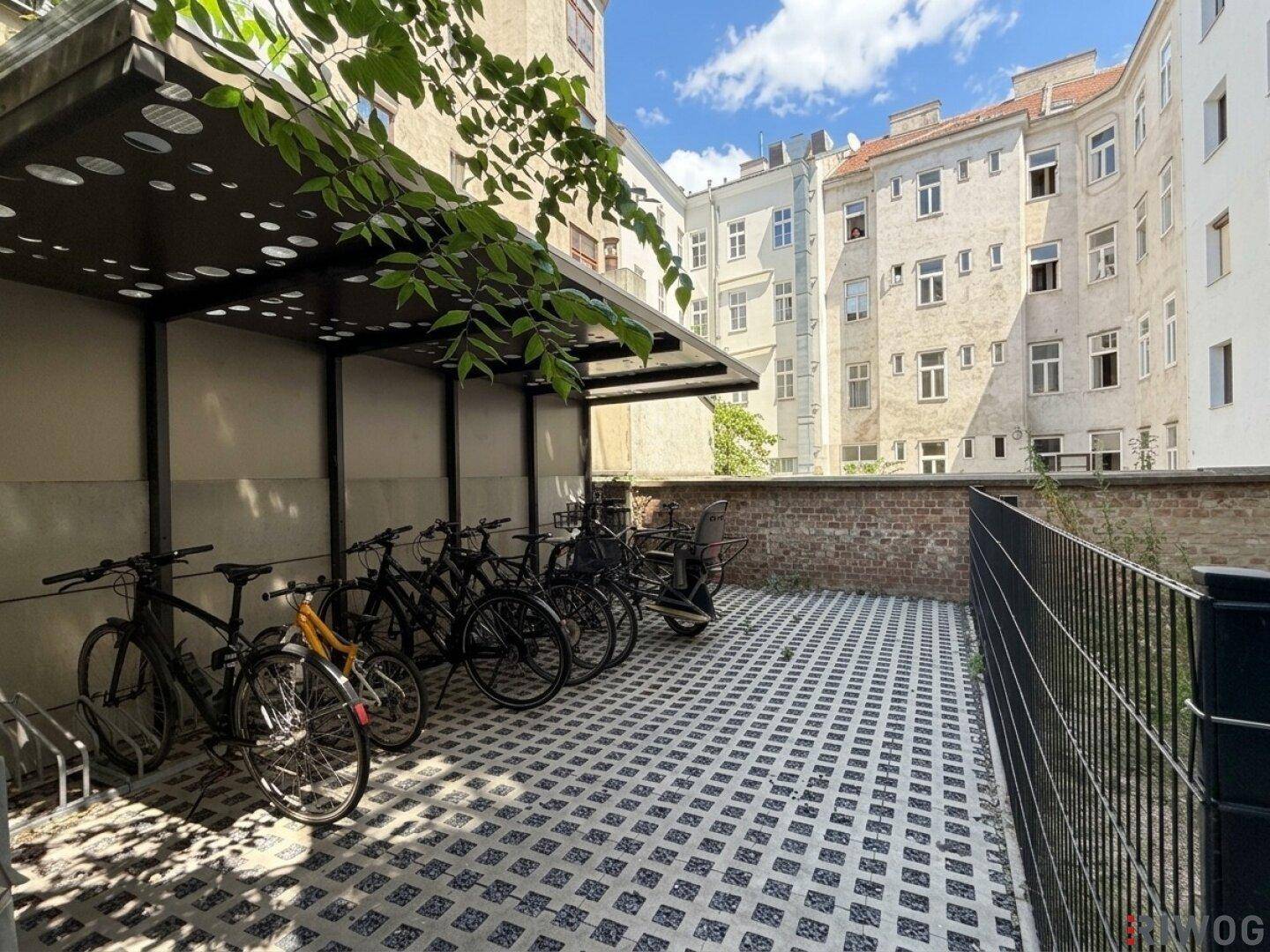 Fahrradabstellplatz im Innenhof mit Überdachung und gepflastertem Untergrund, umgeben von Gebäuden.
