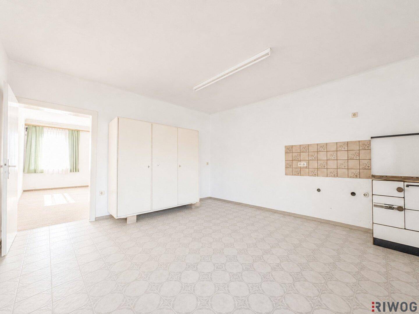 Geräumige Küche mit Fliesenboden, weißen Schränken und vorbereiteten Anschlüssen.