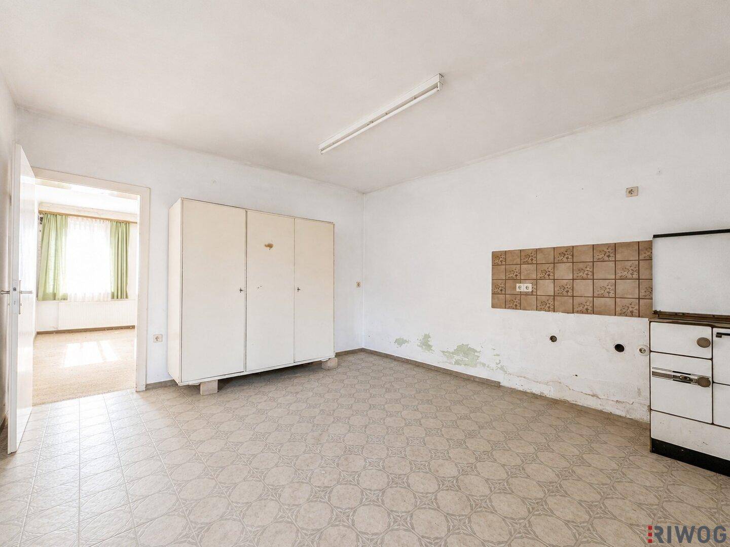 Einfache Küche mit Fliesenboden, Wandfliesen und einem Blick in den Nebenraum.