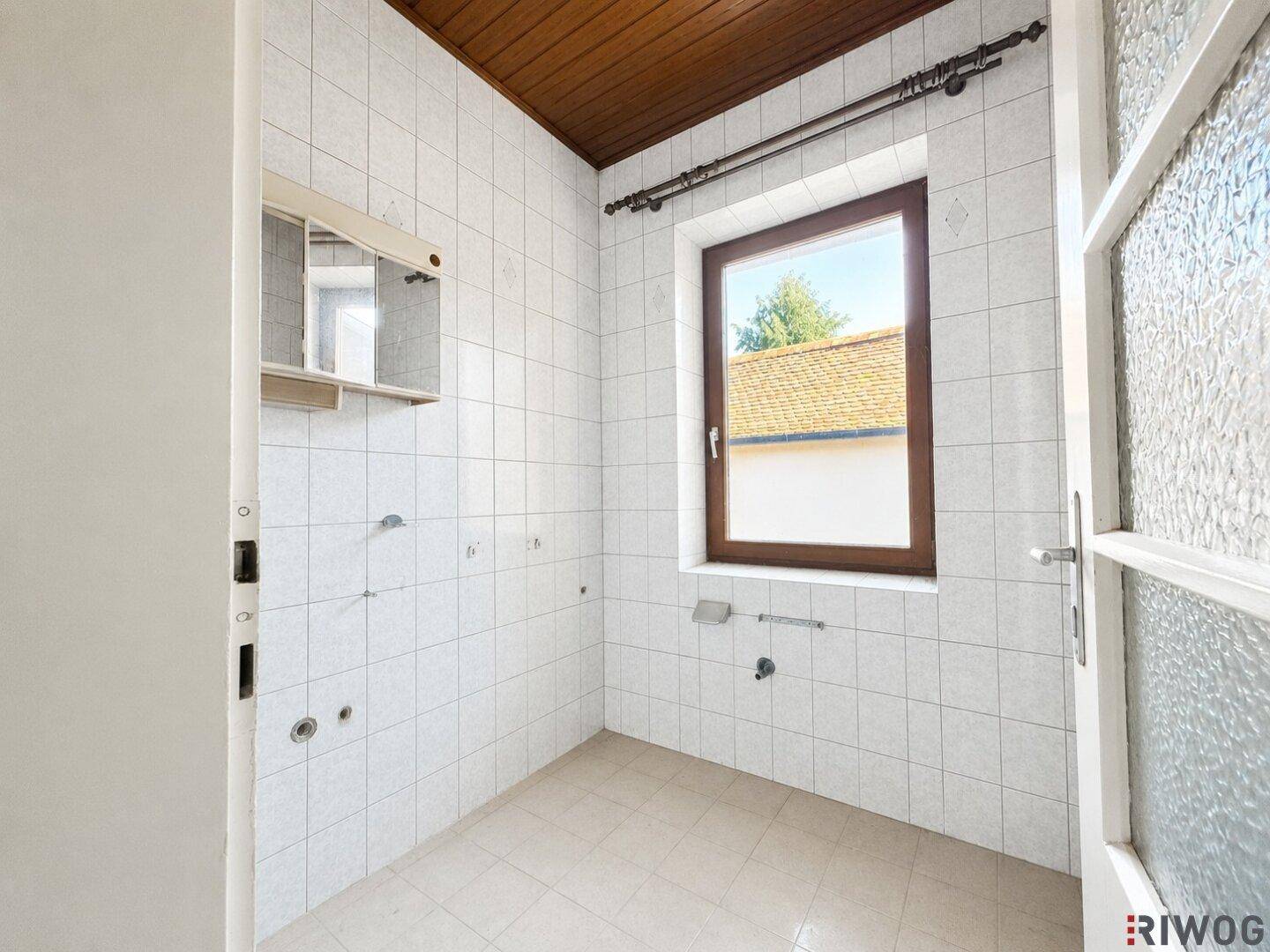 Leeres Badezimmer mit weißen Wandfliesen, Fenster und Holzdecke.