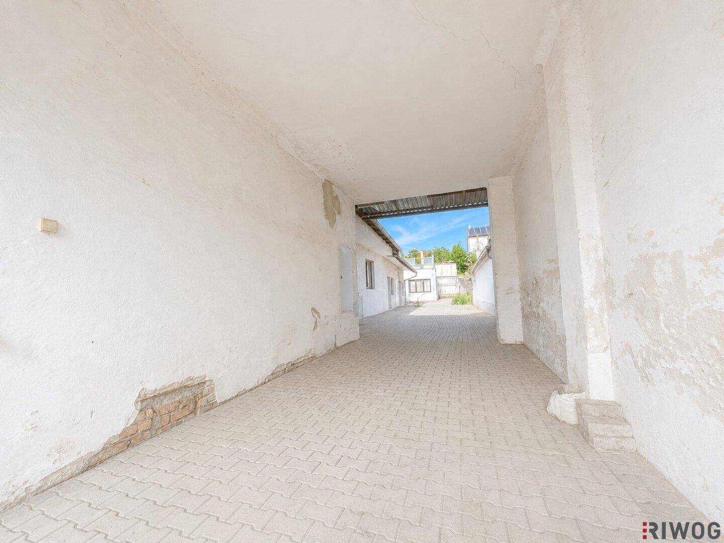 Überdachter Durchgangsbereich mit gepflastertem Boden und Blick auf weitere Gebäude im Hintergrund.