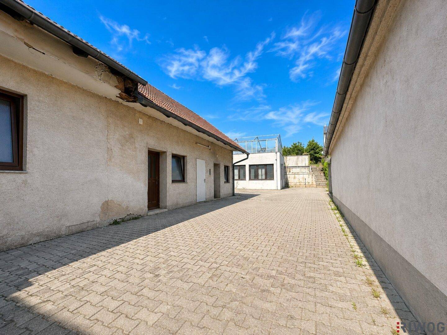 Gepflasterter Außenbereich zwischen Gebäuden mit sonnigem Himmel und Zugangstüren.