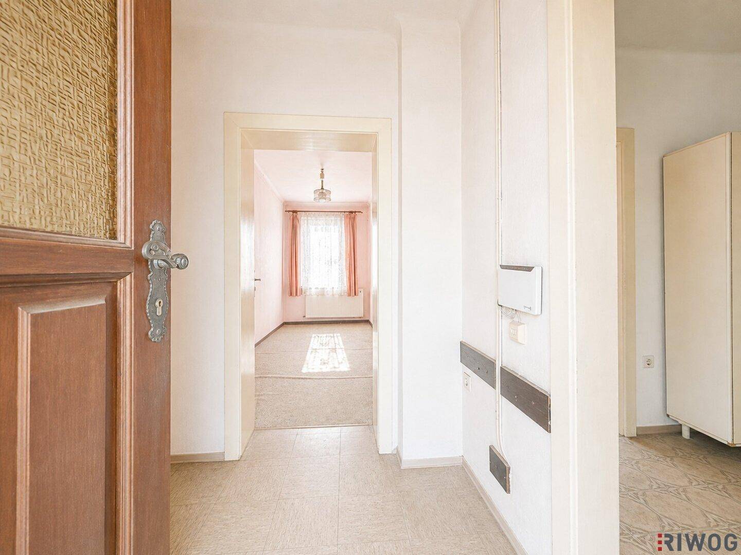 Eingangsbereich mit Holztür, Fliesenboden und Blick in angrenzende Zimmer.