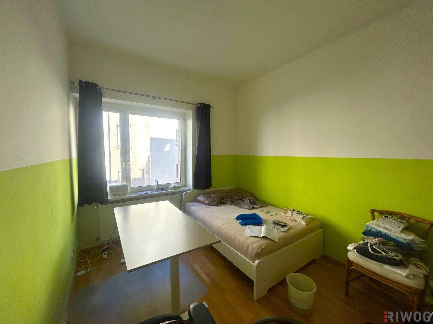 Helles Schlafzimmer mit Einzelbett, Schreibtisch und grün-weißen Wänden.
