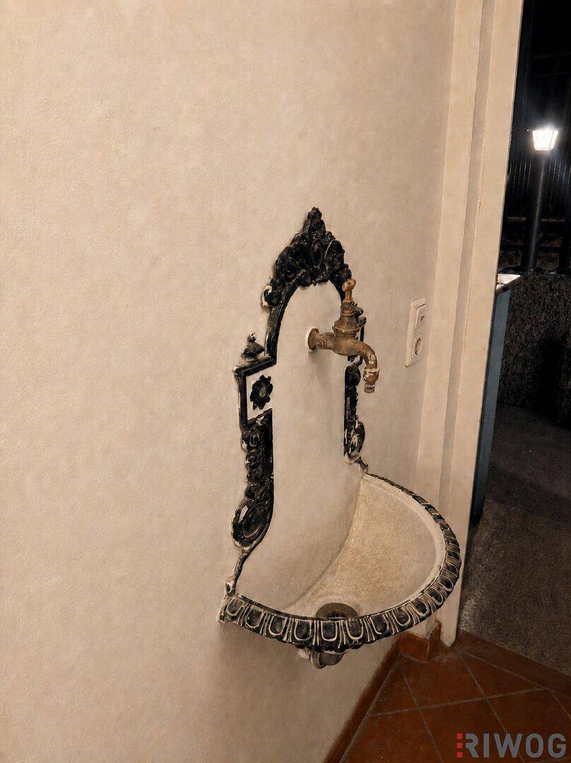 Dekorativer, wandmontierter Brunnen mit antikem Messinghahn und kunstvollen Verzierungen.