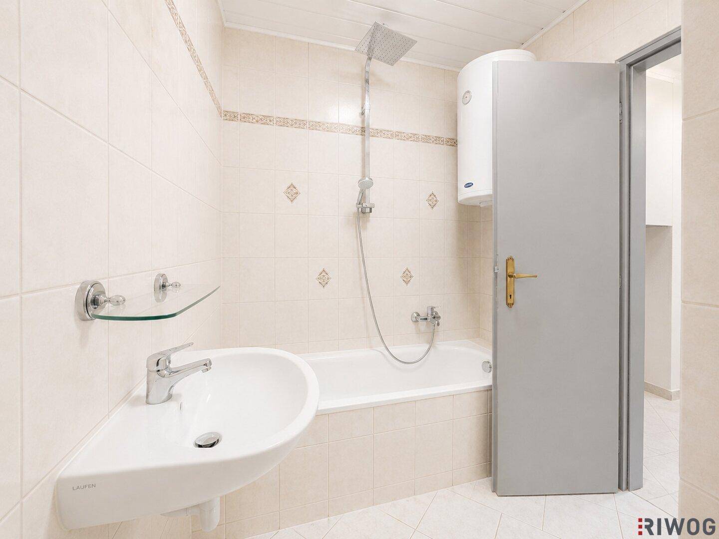Badezimmer mit beigefarbenen Fliesen, Badewanne mit Duschfunktion und einem Waschbecken.