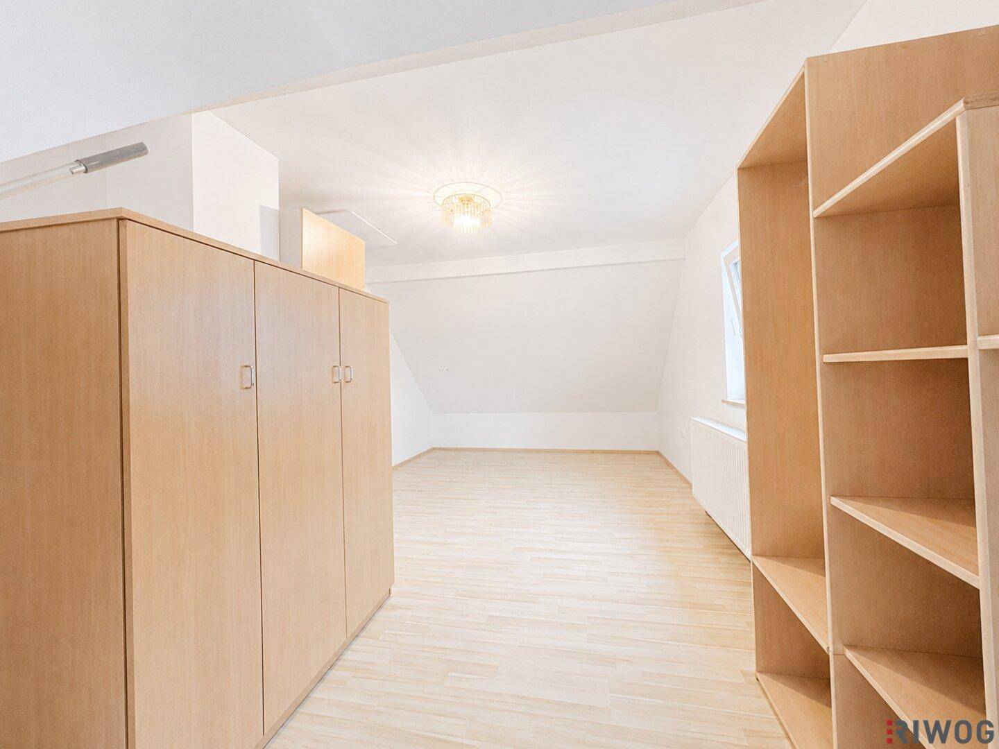 Geräumiger Dachbodenraum mit hellem Holzboden, Dachschrägen und integrierten Holzschränken.