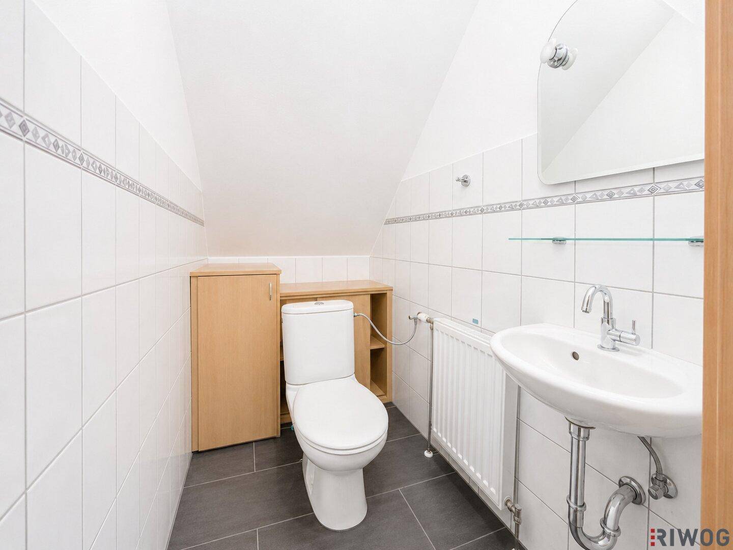 Modernes Badezimmer im Dachgeschoss mit weißen Fliesen, Toilette und Waschbecken unter einer Dachschräge.