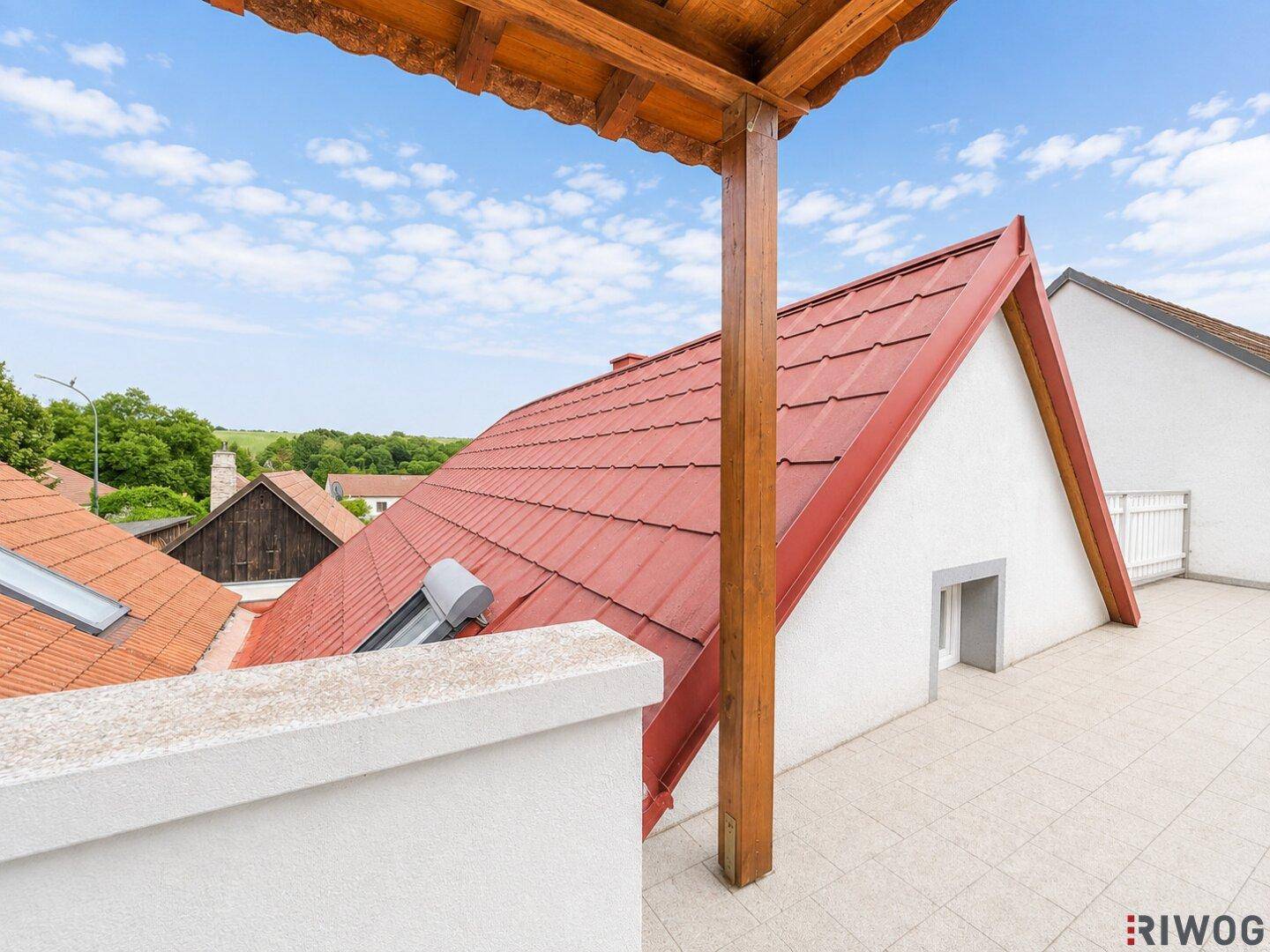 Dachterrasse mit Blick über die roten Ziegeldächer und die grüne Hügellandschaft.