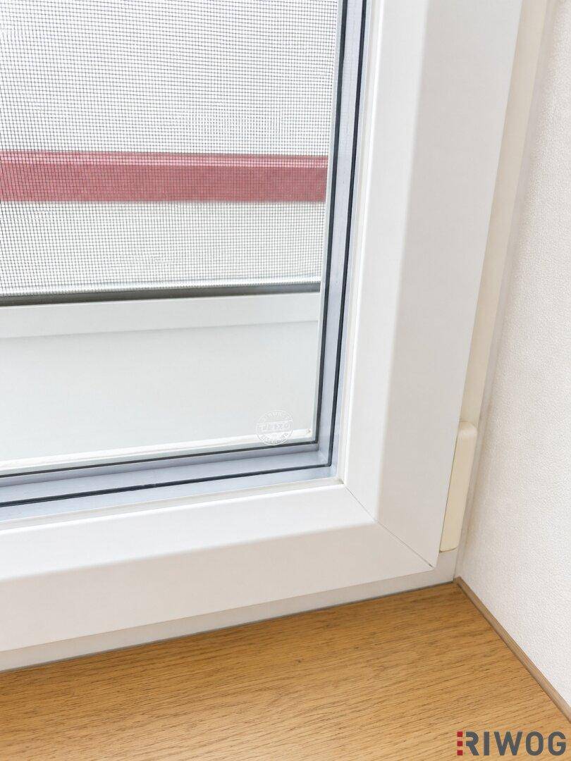 Nahaufnahme eines weißen Fensters mit Fliegengitter und einer hellen Holzfensterbank.