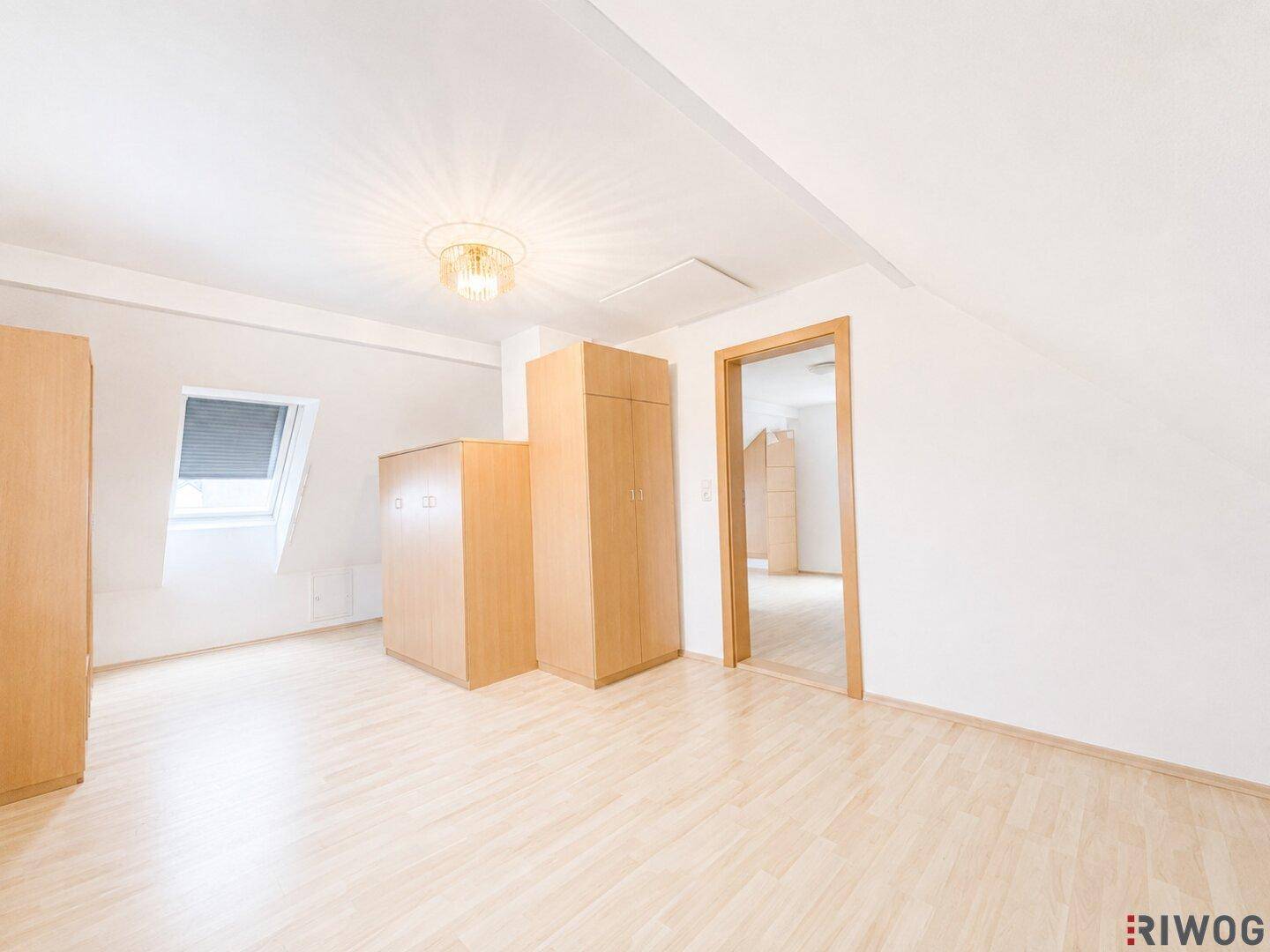 Geräumiger Dachbodenraum mit hellem Holzboden, Dachschrägen und Zugang zu einem weiteren Zimmer.