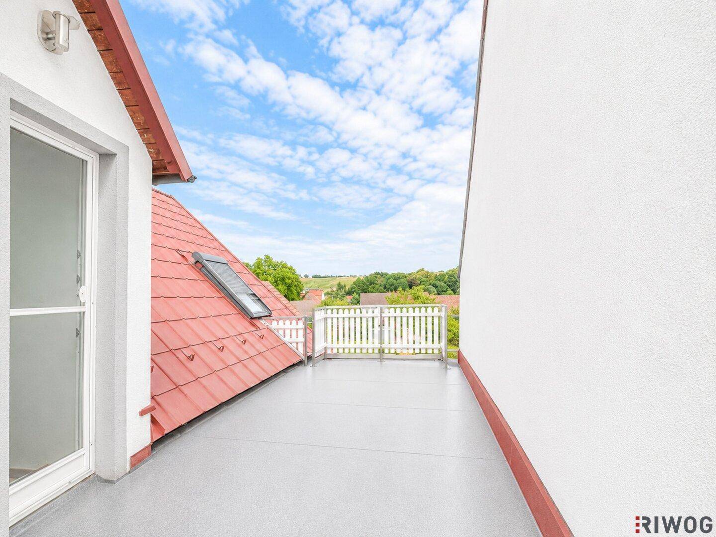Helle Dachterrasse mit grauem Boden, weißem Geländer und weitem Blick über die Landschaft.