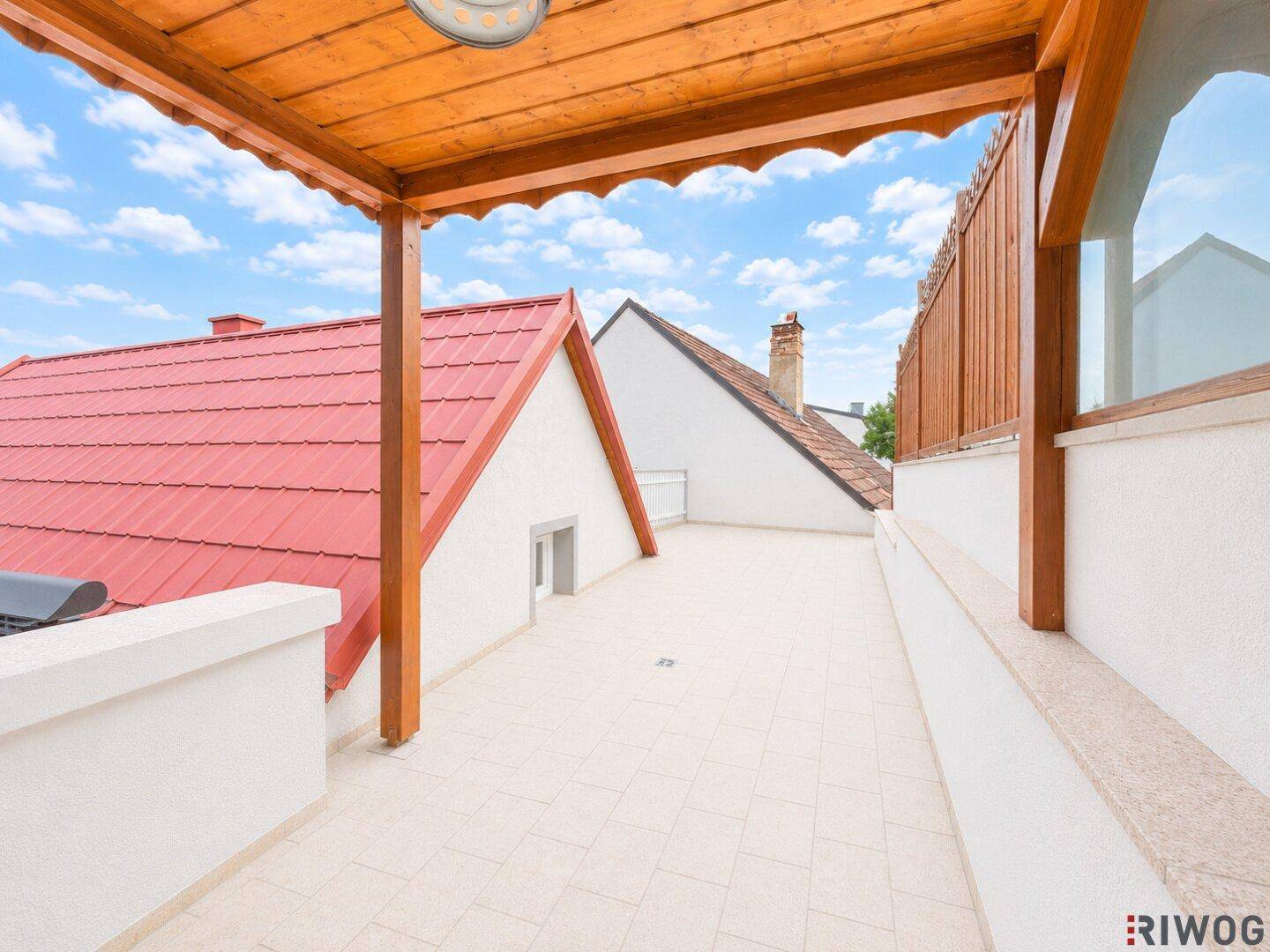 Sonniger Terrassenbereich mit Holzpergola und Blick auf die roten Dächer der Nachbarschaft.