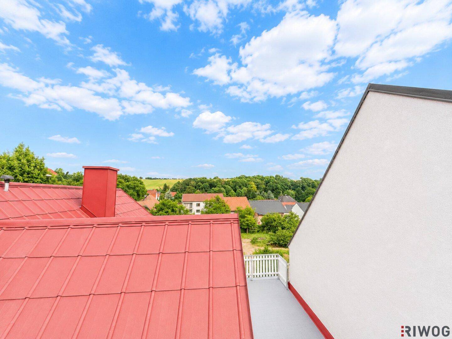 Offene Dachterrasse mit weitem Blick über die grüne Landschaft und die umliegenden Häuser.