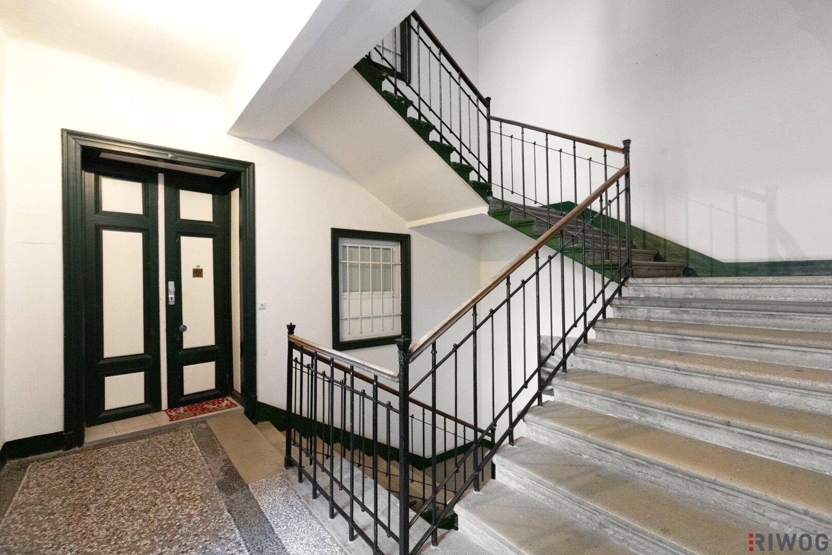 Breites Treppenhaus mit Marmorstufen, schmiedeeisernem Geländer und hohen Decken.
