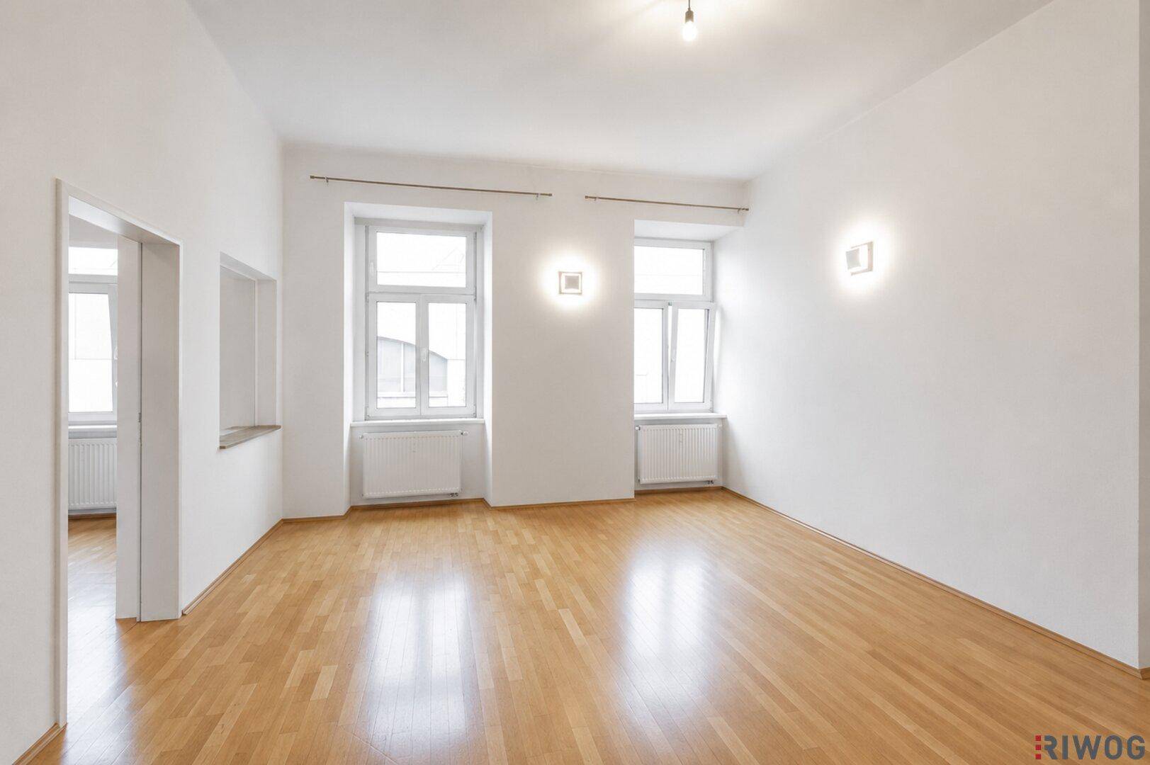 Geräumiger, leerer Raum mit Holzboden, hohen Decken und großen Fenstern.