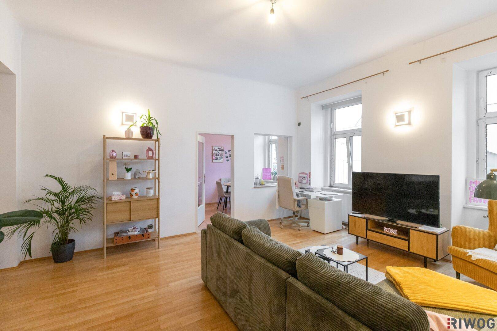 Helles Wohnzimmer mit Holzboden, beigem Sofa und Blick in einen angrenzenden Raum.