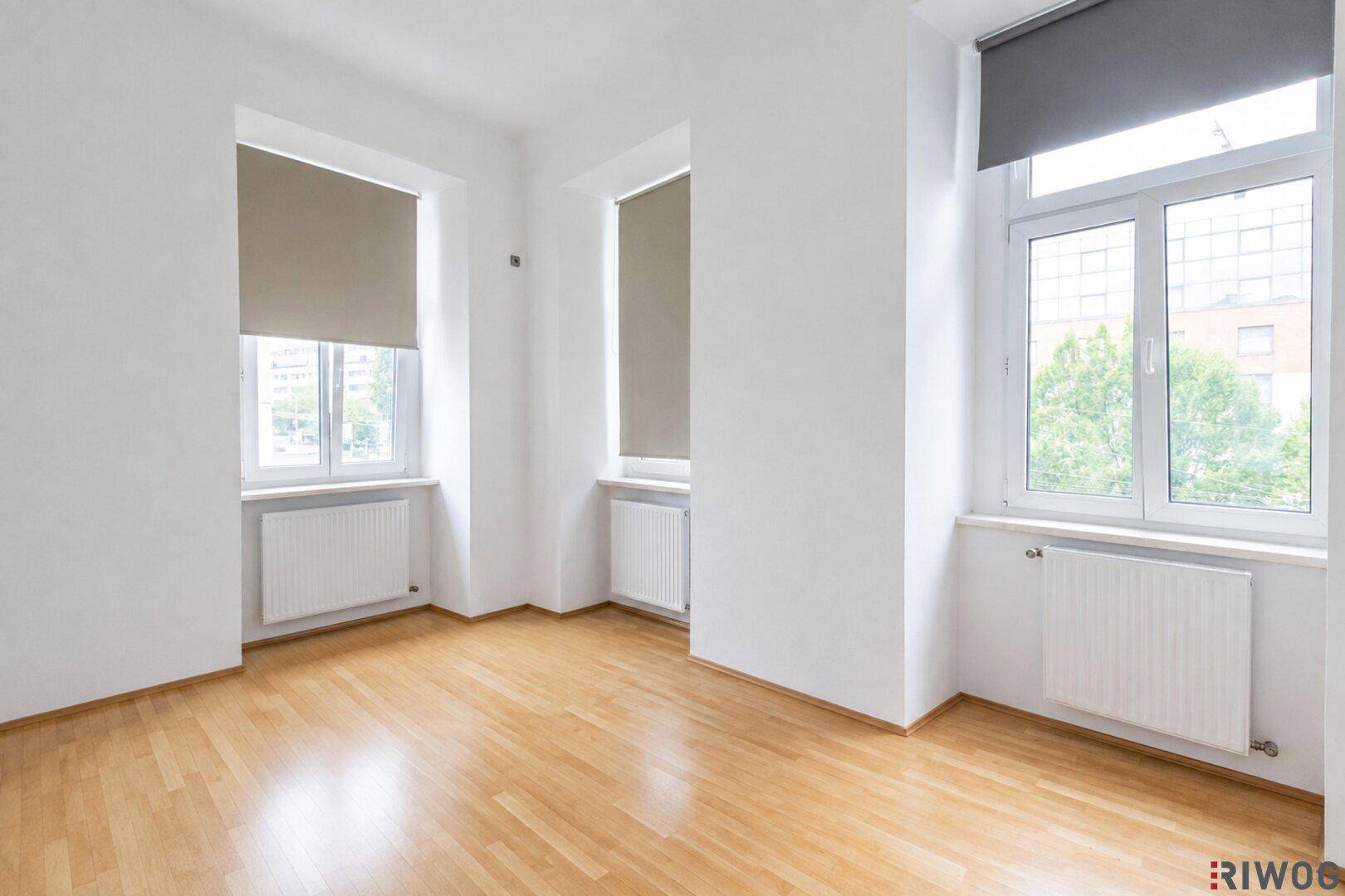 Geräumiges, leeres Schlafzimmer mit Holzboden, hohen Decken und großen Fenstern.