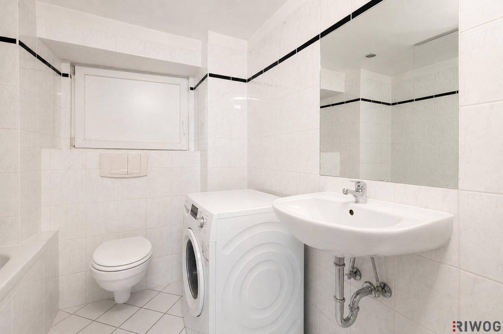 Helles Badezimmer mit weißen Fliesen, Waschmaschine, WC und Waschbecken.